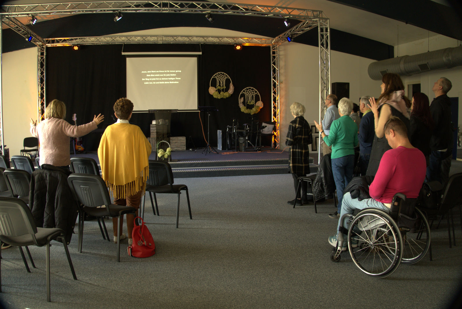Gemeinde im Gottesdienst, Menschen stehen mit erhobenen Händen vor der Bühne